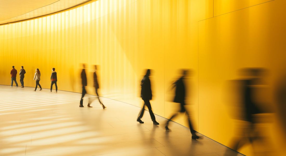 Sonder Blurred motion of people walking in a modern, yellow-colored corridor, creating a dynamic and vibrant scene