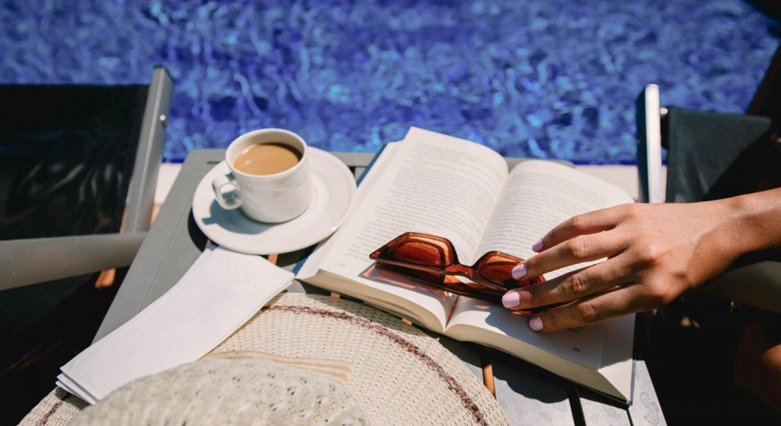 Sonder Coffee and book at the pool side.Female Sits Near By Pool at Summer Time Reading Book Drink Coffee.Cup of coffee and glasses on open book on table