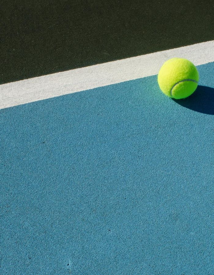 Sonder A bright yellow tennis ball rests on a blue court, close to a white line, with a dark green surface in the background.