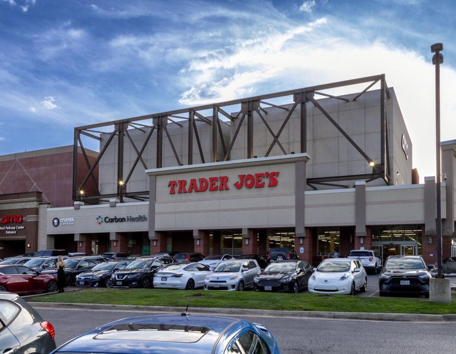 Trader Joe’s storefront with several cars parked in front under a partly cloudy sky.