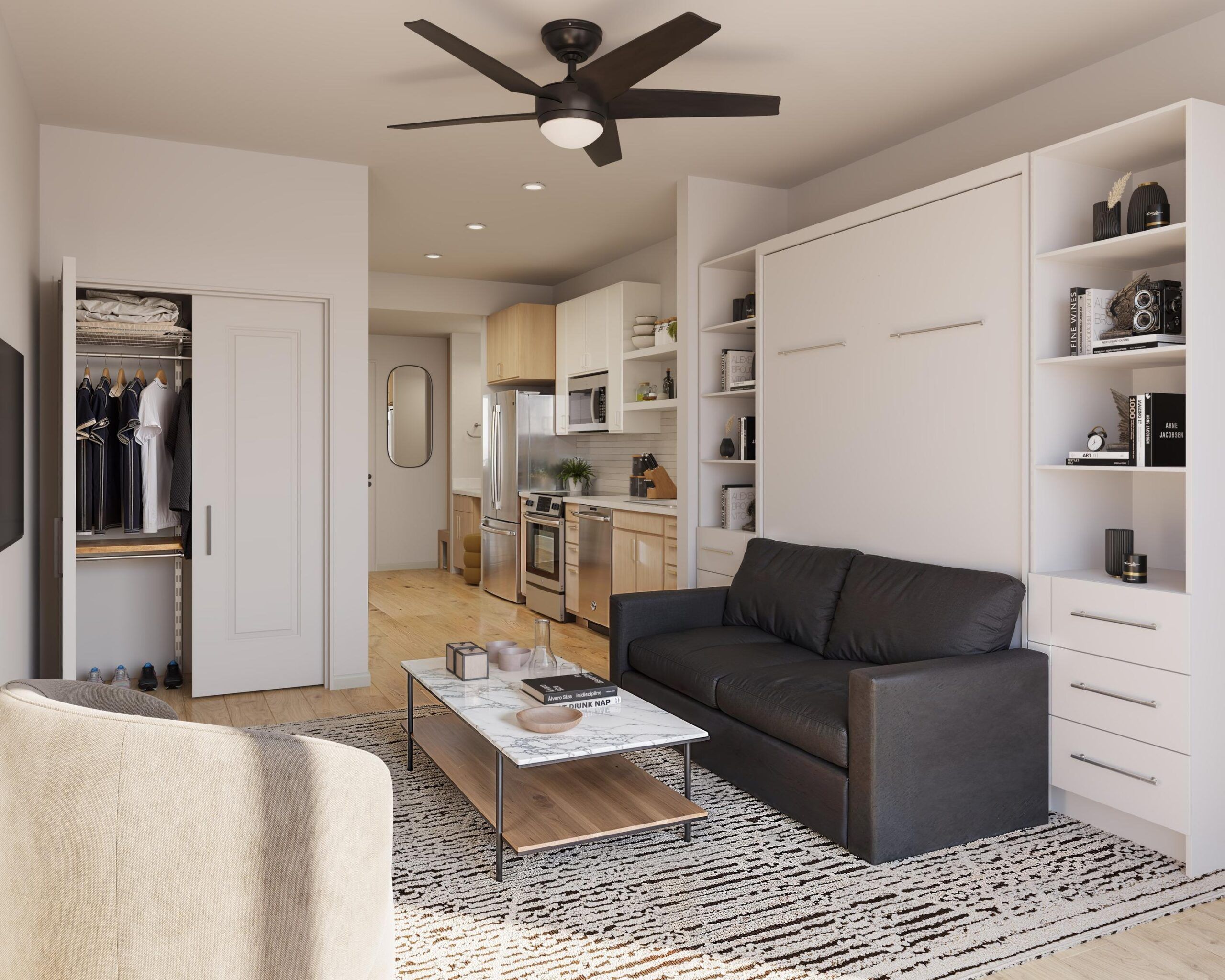 Modern studio apartment with a black sofa, built-in shelves, kitchen area, and ceiling fan.